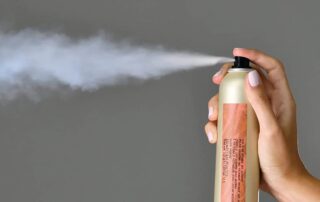 A photo of a hand spraying a can of dry shampoo